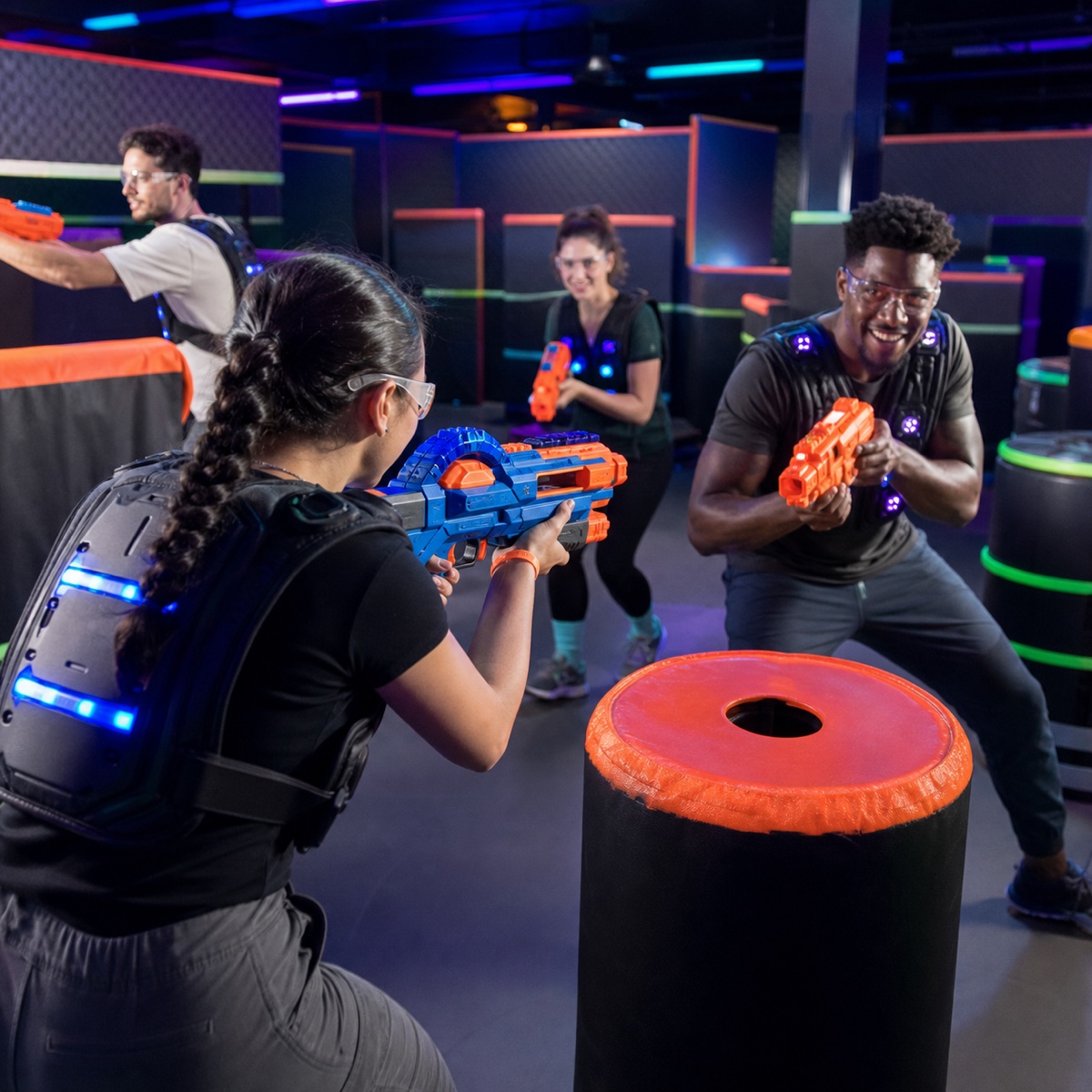 Friends playing with foam-dart blasters in a laser tag arena